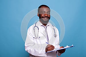 Confident smiling doctor posing in white lab coat with stethoscope holding clipboard
