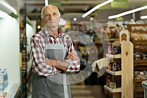 Confident smiling elderly supermarket clerk posing at the shopping mall, looking to the camera. Retail job concept.