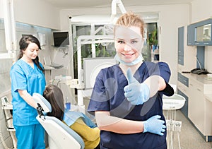 Confident smiling female dentist thumb up in her dental office