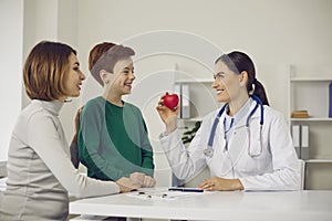 Confident smiling woman pediatrician showing happy heart to positive boy teen patient and his mother