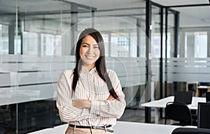 Confident smiling young Asian business woman standing in office, portrait.