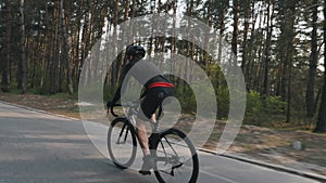 Confident strong triathlete pedaling on bicycle in the park as a park of his training schedule for a race. Triathlon concept. Slow