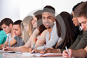 Confident student sitting with classmates writing at desk