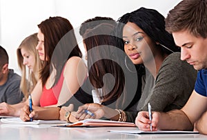 Confident student sitting with classmates writing at desk