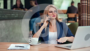 Confident stylish business female talking using smartphone sitting on table in cafe