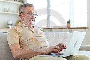 Confident stylish happy middle aged senior man using laptop at home. Stylish older mature 60s beard grandfather sitting