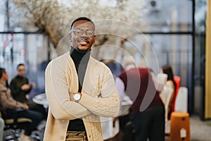 Confident and successful black businessman standing and posing in modern office with smile and satisfaction on his face.