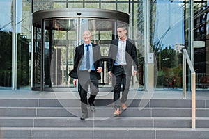 Confident and successful business men walking down the staircase, talking about the corporate finance. Office colleagues