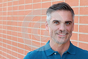 Confident and successful. Cheerful mature man in blue polo shirt looking at camera while standing against brick wall urban