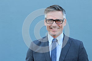 Confident and successful. Cheerful mature man in suit, shirt and tie looking at camera while standing against blue background