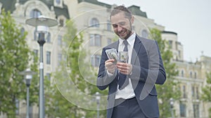 Confident successful rich businessman counting dollars and smiling. Portrait of happy Caucasian young man with money