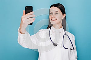 Confident and successful woman doctor or medic taking selfie with smartphone, using mobile app, making video for social network