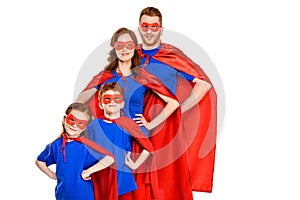 confident super family in masks and cloaks standing with hands on waist and smiling at camera