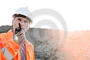 Confident supervisor using walkie-talkie on construction site against clear sky