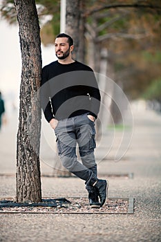 Confident Tough Handsome Man Posing, leaning against a tree