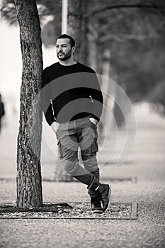 Confident Tough Handsome Man Posing, leaning against a tree