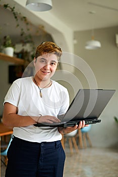 Confident transgender employee holds laptop in modern office cafe. Short-haired, smiling FTM pro in casual wear photo