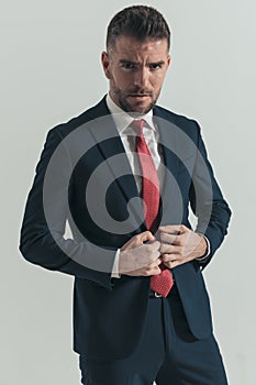 Confident unshaved man with beard buttoning elegant suit