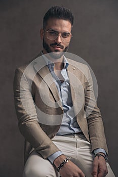 Confident unshaved man with eyeglasses in beige suit sitting