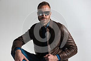 Confident unshaved man wearing brown leather jacket and sunglasses