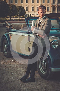 Confident wealthy man with newspaper near classic convertible