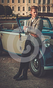 Confident wealthy man with newspaper near classic convertible