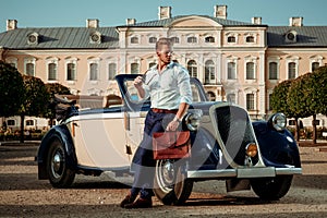 Confident wealthy young man with briefcase near classic convertible photo