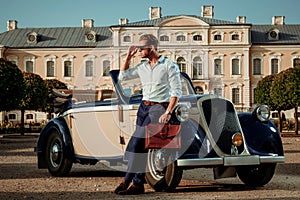 Confident wealthy young man with briefcase near classic convertible