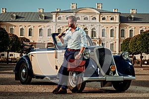 Confident wealthy young man with briefcase near classic convertible