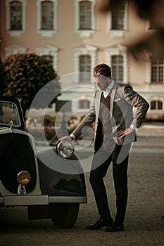 Confident wealthy young man near classic convertible