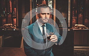 Confident well-dressed man with glass of whisky in Luxury apartment interior.