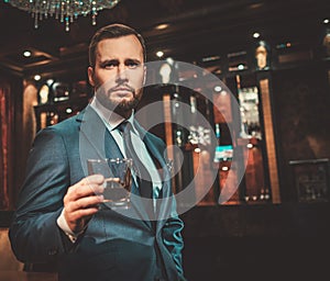 Confident well-dressed man with glass of whisky in luxury apartment interior.