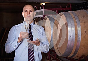 Confident winemaker offering glass of white sparkling wine for tasting in wine cellar