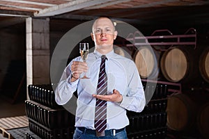 Confident winemaker offering glass of white sparkling wine for tasting in wine cellar