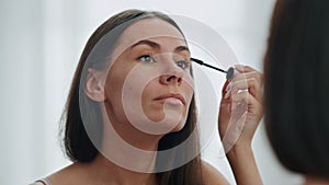 Confident woman applying mascara mirror place. Beautiful model preparing makeup