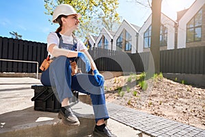 Confident woman building engineer in hardhat and overall sitting and resting