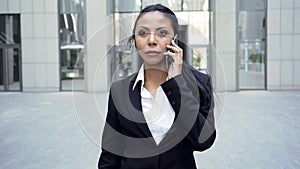 Confident woman in business suit walking, holding phone by ear, conversation