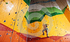 Confident woman climbing up the orange wall in gym