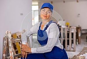 Confident woman construction worker in blue overalls in house under renovation