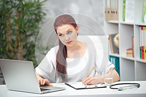 Confident woman doctor sitting at the table in her office and works at the computer. healthcare concept