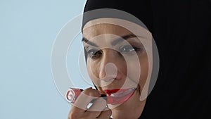 Confident woman in hijab applying red lipstick in front of mirror, make-up