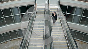 Confident woman is reading e-mail in internet via mobile phone, while is standing in shopping center on escalator
