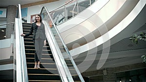 Confident woman is reading e-mail in internet via mobile phone, while is standing in shopping center on escalator