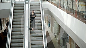 Confident woman is reading e-mail in internet via mobile phone, while is standing in shopping center on escalator