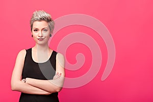 Confident woman standing with arms crossed over pink background photo