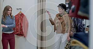 Confident woman standing in shop dressing room as young female shopper opening curtain and going out. mother admiring