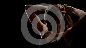 Confident woman taking hair into ponytail against dark background, female power