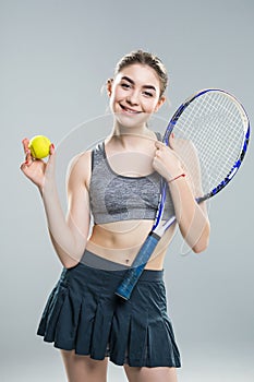 Confident woman tennis player holding racket and ball isolated over gray background