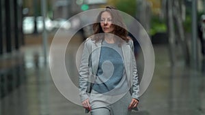 Confident woman is walking on city street, looking at camera and going forward, contemporary female city dweller
