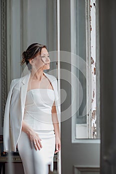 a, confident woman in a white suit at the old window. image of bride